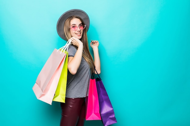 Bella donna dello shopping sorridente e indossa un cappello isolato su sfondo verde