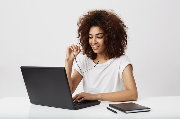 Bella donna di affari africana che esamina lo schermo del computer portatile sopra la parete bianca.