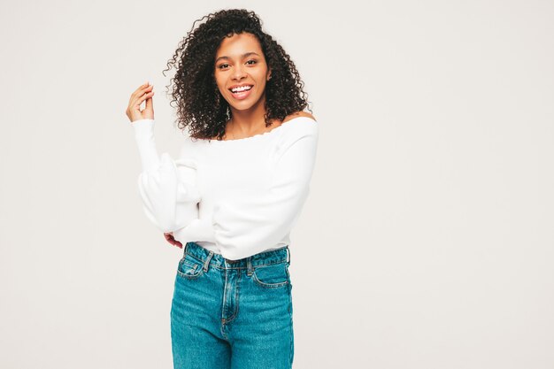 Bella donna di colore con l'acconciatura di riccioli afro. Modello sorridente in maglione e vestiti di jeans alla moda