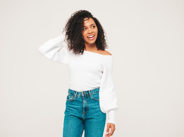 Bella donna di colore con l'acconciatura di riccioli afro. Modello sorridente in maglione e vestiti di jeans alla moda