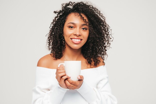 Bella donna di colore con l'acconciatura di riccioli afro. Modello sorridente in maglione e vestiti di jeans alla moda