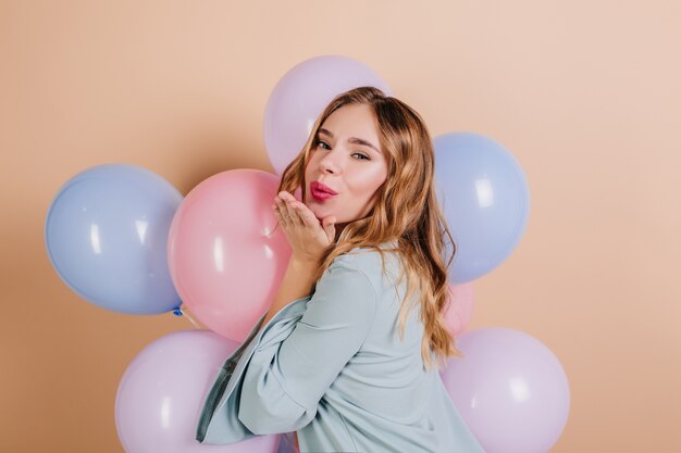 Bella donna di compleanno con capelli ondulati in posa sulla parete chiara