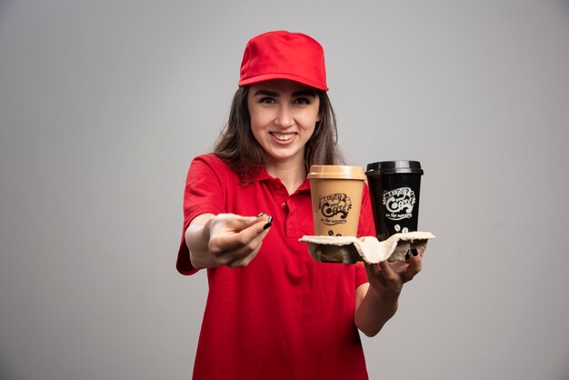 Bella donna di consegna in rosso in posa sul muro grigio.