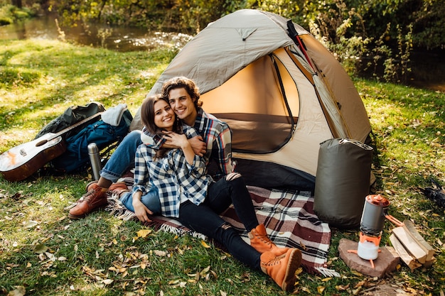 Bella donna e bell'uomo che trascorrono del tempo sulla natura, seduti vicino alla tenda sul plaid