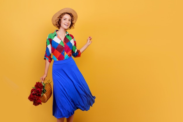 Bella donna europea in abito blu tenendo il mazzo di fiori su sfondo giallo. Cappello di paglia. Atmosfera estiva.