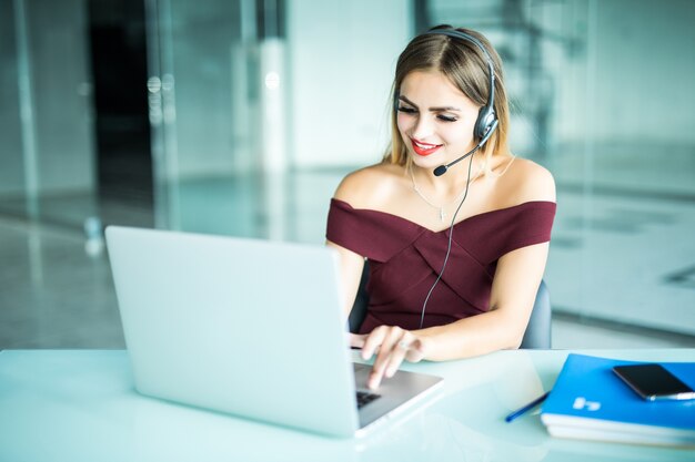 Bella donna freelance parlando in una videoconferenza in linea con un auricolare con microfono e laptop in un desktop da ufficio o da casa