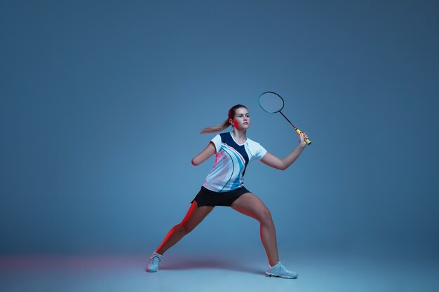 Bella donna handicap praticando nel badminton isolato su sfondo blu in luce al neon. Stile di vita di persone inclusive, diversità ed equità. Sport, attività e movimento. Copyspace per annuncio.