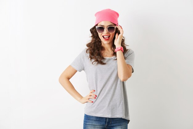 Bella donna hipster con cappello rosa, occhiali da sole, sorridente, isolato, denti bianchi, labbra rosse, capelli ricci, indossa la maglietta