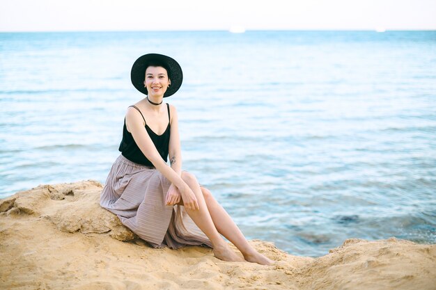 Bella donna in cappello nero e camicia seduta e sorridente.