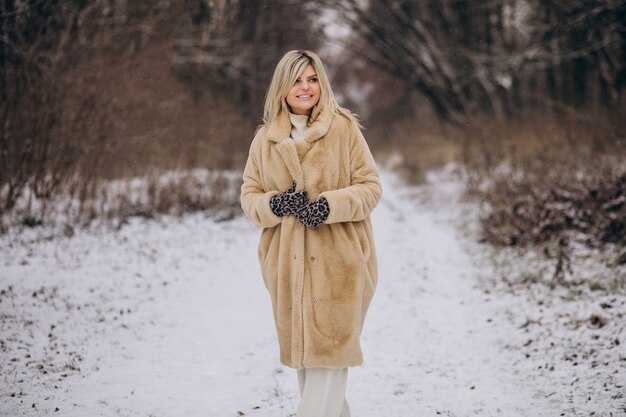 Bella donna in cappotto invernale che cammina nel parco pieno di neve