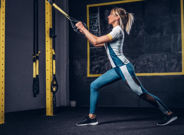 Bella donna in forma in abbigliamento sportivo che fa esercizio con sistema di cinghie di sospensione in palestra.