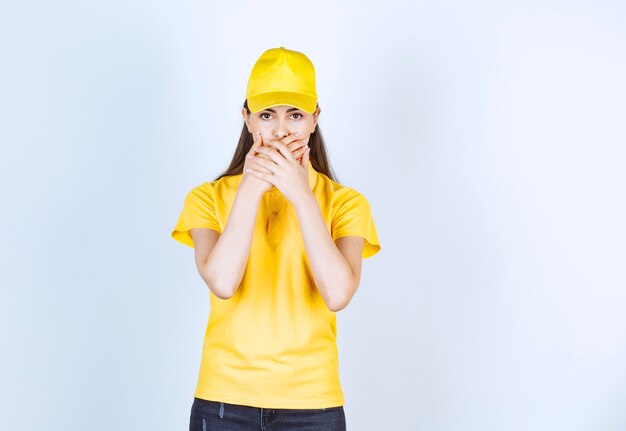 Bella donna in maglietta gialla e berretto scioccata per qualcosa su sfondo bianco.