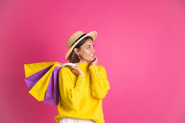 Bella donna in maglione giallo brillante e cappello di paglia su borse della spesa rosa tenere felice eccitato gioioso spazio isolato per il testo