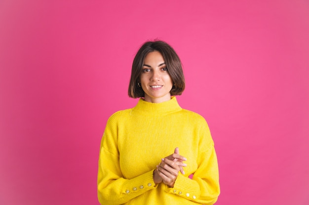 Bella donna in maglione giallo brillante isolato su rosa guarda davanti con un sorriso fiducioso