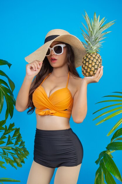 Bella donna in un costume da bagno che tiene un ananas sul blu