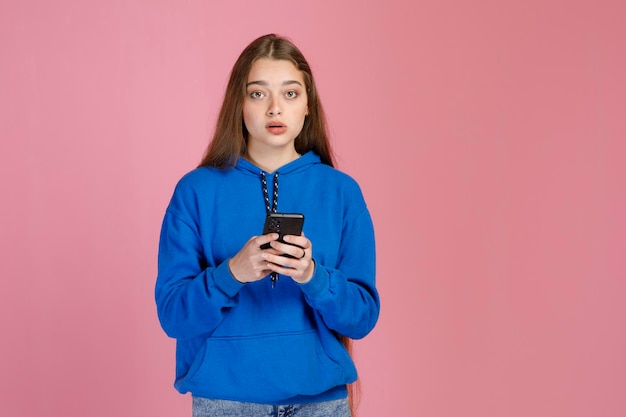 Bella donna interessata in abiti casual che tiene smartphone e guarda con ansia la fotocamera