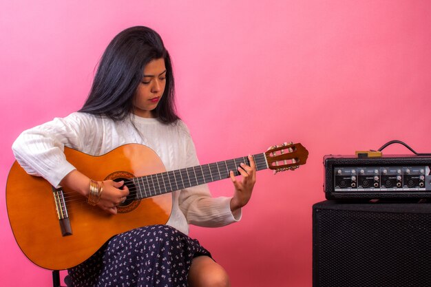 Bella donna latina che suona la chitarra con un muro rosa in scena