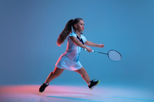 Bella donna nana che pratica a badminton isolata sul blu alla luce al neon