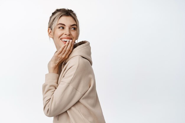 Bella donna naturale, sorridente, ridente e con il suo sorriso con la mano, guardando felice dietro la spalla su bianco