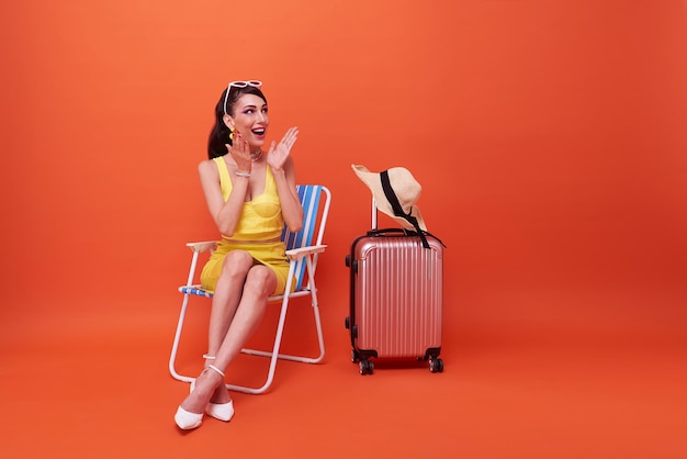 Bella donna rilassarsi seduto su una sedia a sdraio con la valigia in studio estate sfondo arancione