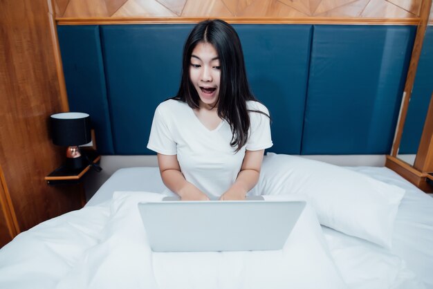 Bella donna scossa che utilizza computer portatile che compera online sul letto