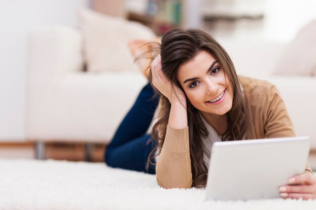 Bella donna sdraiata sul tappeto e utilizzando la tavoletta digitale