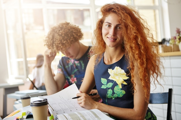 Bella donna seduta al coffe shop facendo esercizi nel suo quaderno