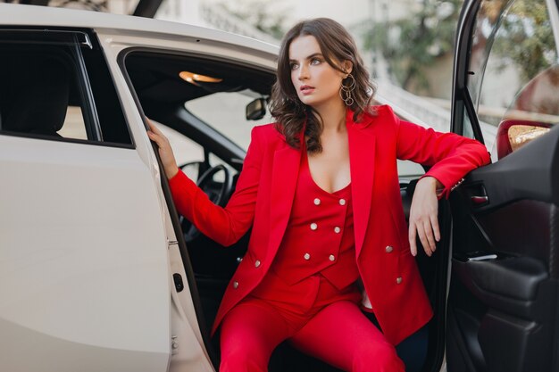 Bella donna sexy ricca di affari in vestito rosso che posa in macchina bianca