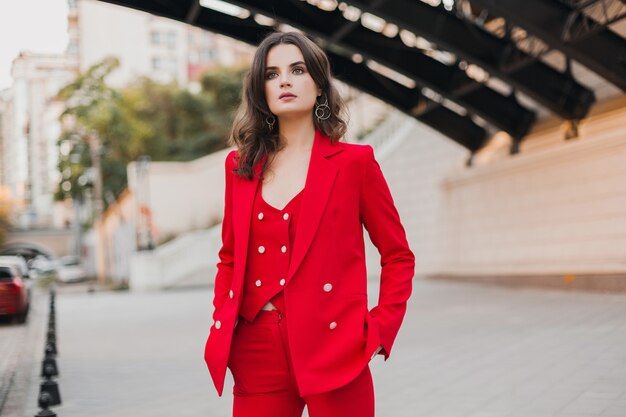 Bella donna sexy ricca di stile di affari in vestito rosso che cammina nella via della città, tendenza della moda primavera estate