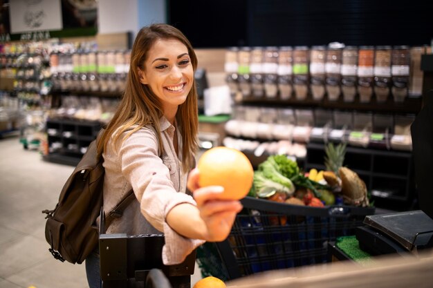 Bella donna sorridente acquisto di arance in un supermercato al reparto frutta