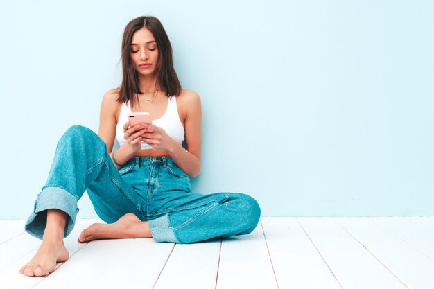 Bella donna sorridente vestita di maglia bianca e jeans. modello allegro spensierato usando il suo smartphone