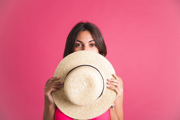 Bella donna sportiva abbronzata in forma in bikini e cappello di paglia sul rosa