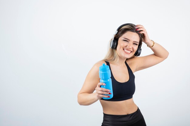 Bella donna sportiva in cuffie che tengono bottiglia con acqua.