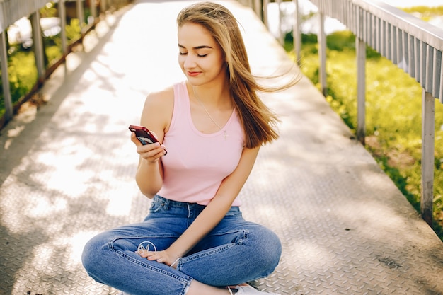 bella e brillante ragazza in t-shirt rosa e blue jeans seduto nel parco soleggiato estate