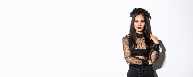 Bella e impertinente donna asiatica vestita con abito di pizzo nero e corona per la festa di halloween wi femminile