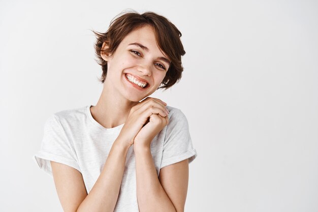 Bella e tenera ragazza senza trucco, sorridente e guardando qualcosa di adorabile e carino, muro bianco