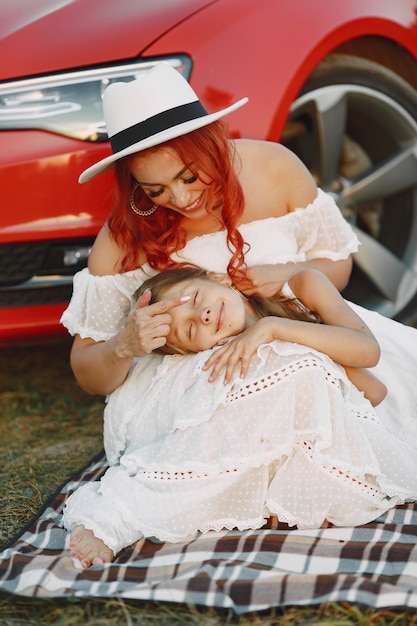 Bella famiglia in un parco. Donna in abito bianco e cappello. Madre con la figlia che si siede sulla coperta.