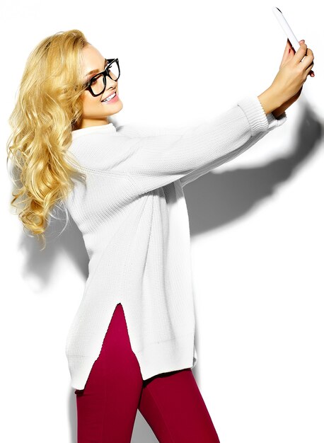 bella felice dolce carina donna bionda sorridente in abiti casual caldo maglione bianco hipster, in bicchieri prendendo selfie