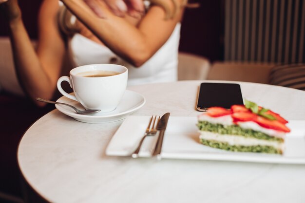 Bella femmina caucasica con lunghi capelli biondi ondulati si siede sul divano, beve caffè drinks