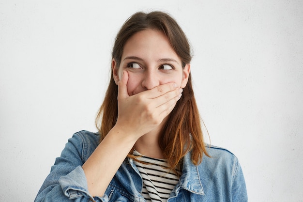 Bella femmina che copre la bocca mentre ridacchia guardando da parte in posa