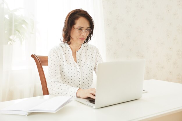 Bella femmina matura asiatica che per mezzo del computer portatile portatile