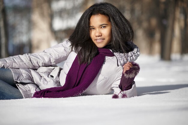 Bella femmina nera americana sorridente che si trova nella neve all'aperto