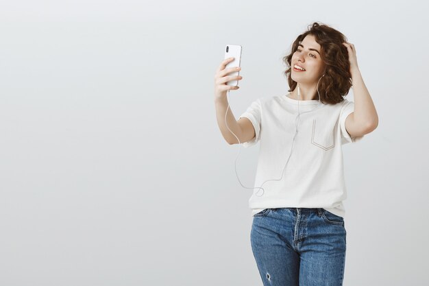 Bella femmina prendendo selfie mentre si ascolta la musica in auricolari