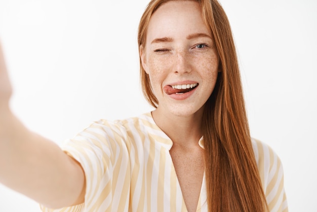 Bella femmina rossa femminile con graziose lentiggini ammiccanti che attacca fuori la lingua civettuola e prendendo con gioia selfie