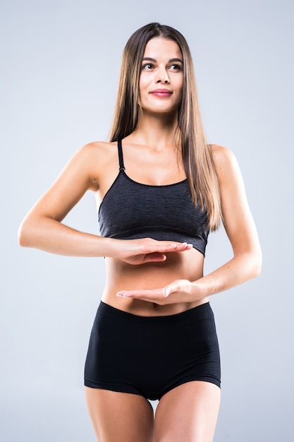 Bella forma del cuore di gesto di mano della donna del ritratto sulla pancia, abbigliamento di sport d'uso della ragazza con l'esercizio isolato su bianco.