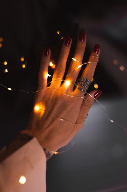 Bella foto scura delle dita della mano della donna con un grande anello d'argento su fiori e luci incandescenti