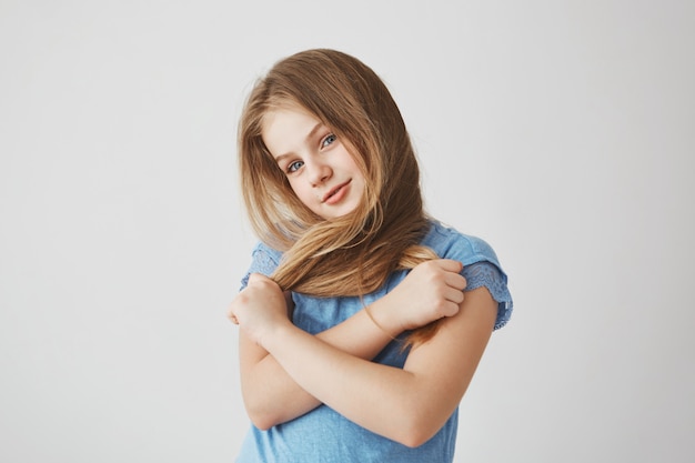 Bella gioiosa ragazza dai capelli chiari in camicia blu, con espressione faccia buffa, tenendo i capelli con le mani e attraversandolo.