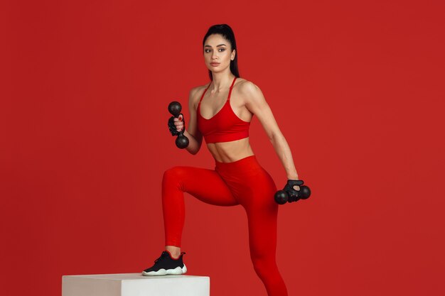 Bella giovane atleta femminile che si esercita sul ritratto monocromatico della parete rossa