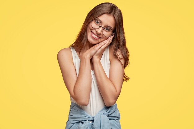 bella giovane bruna con gli occhiali in posa contro il muro giallo