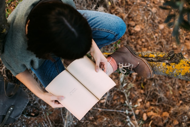 Bella giovane bruna seduta su un autunno caduto foglie in un parco, leggendo un libro